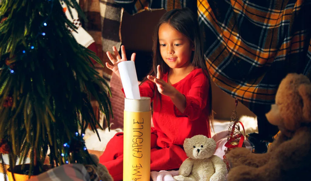 Cute little child girl writes the letter and putting into time capsule with Christmas decoration at home