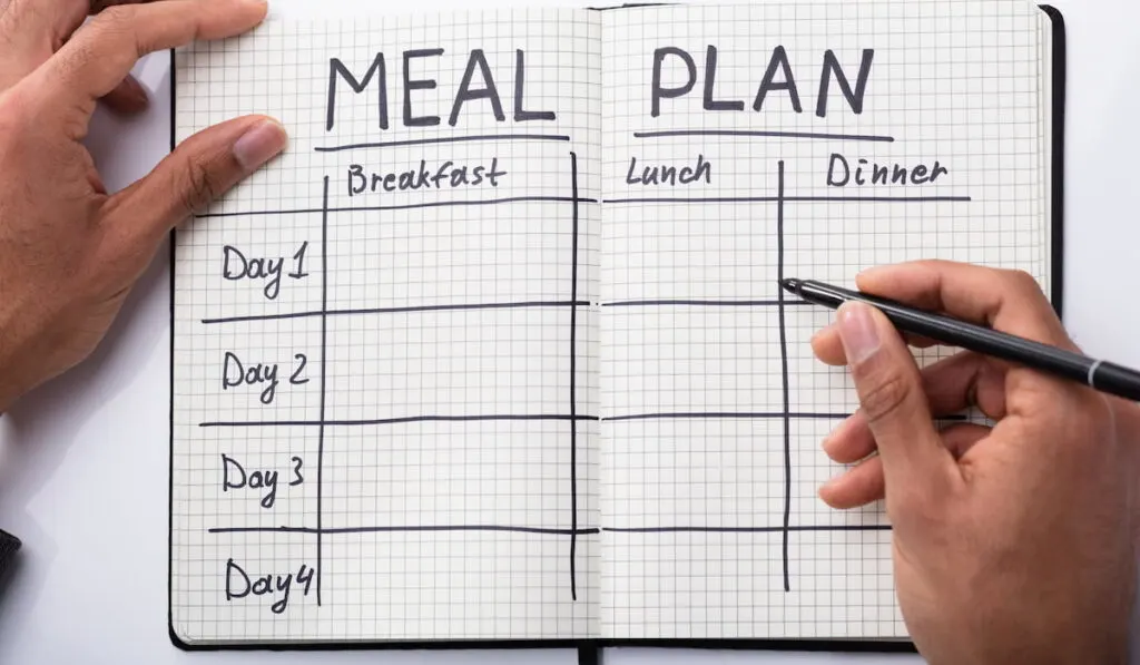 man filling in his meal plan on his notebook for the week