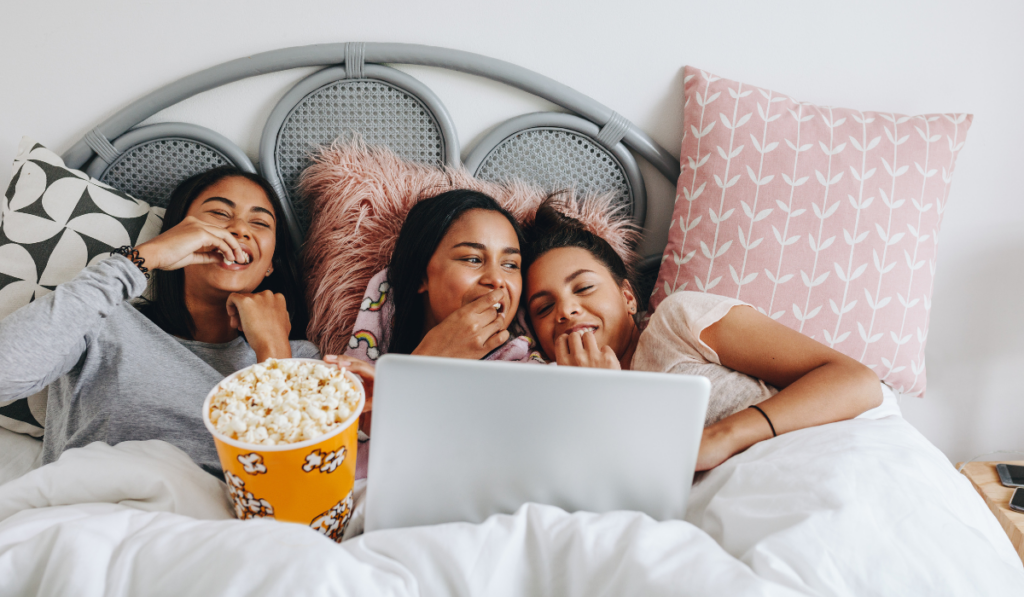 girls having a sleepover enjoying a movie on laptop with popcorns