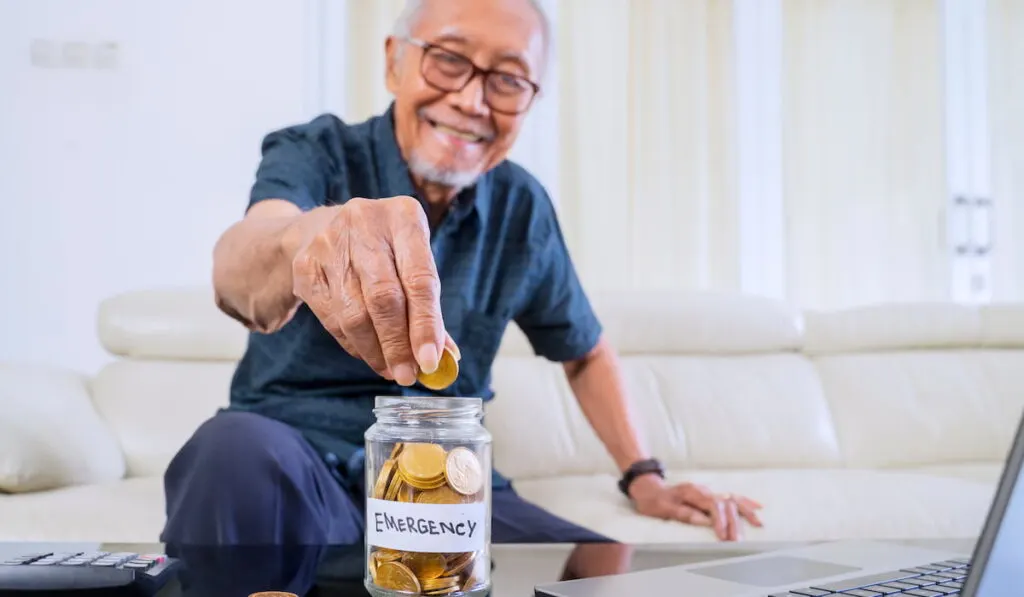 senior man putting money in his emergency fund jar