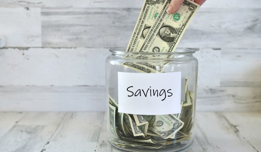 Woman putting dollars in a jar labelled Savings