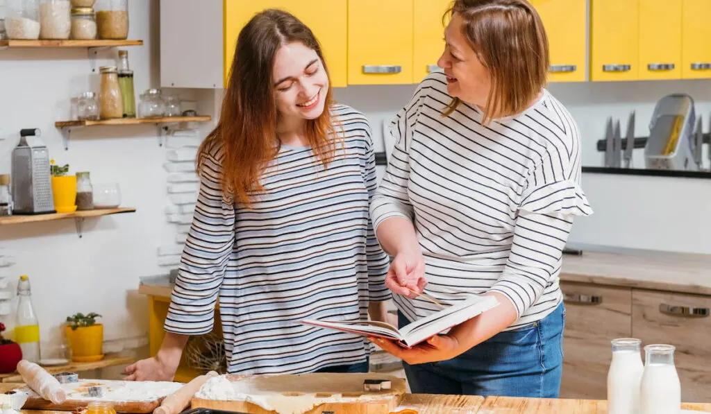 Mother and daughter using recipe from cookery book to make biscuits 