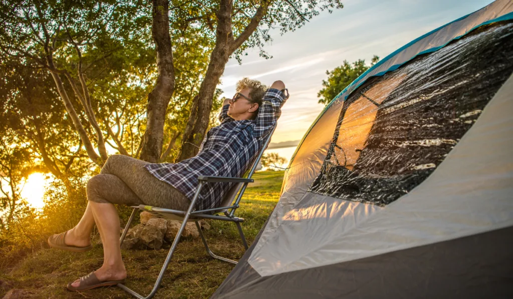 Old Woman resting enjoying sunset near lake and her tent 