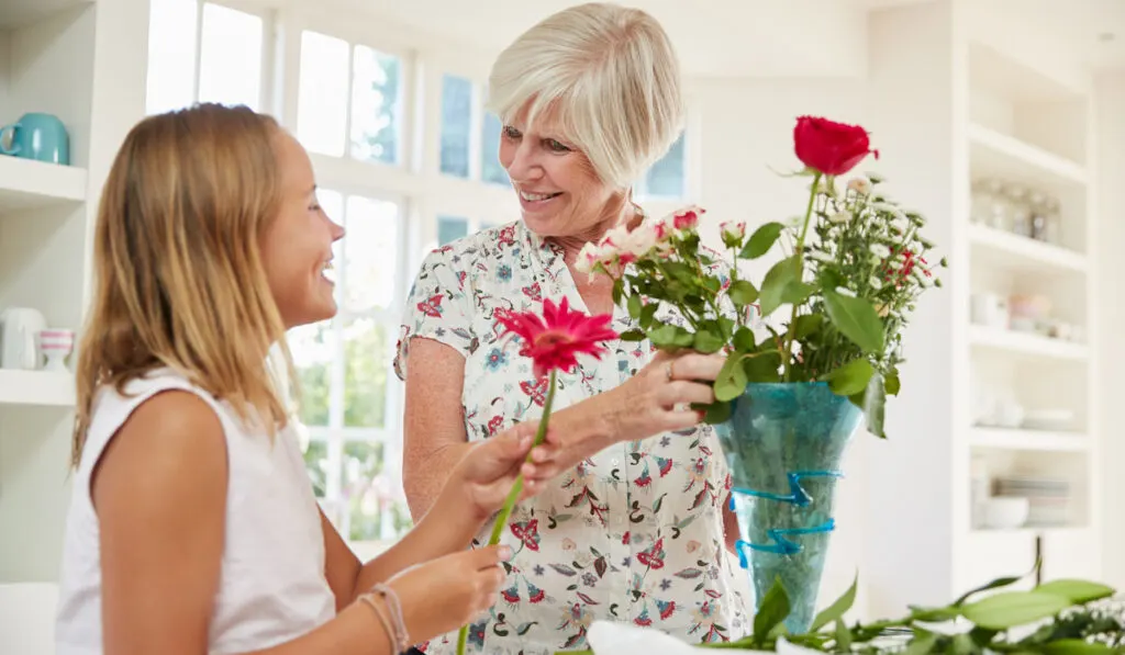 Senior woman arranging flowers with granddaughter at home
