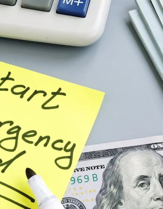 start an emergency fund written on a sticky notepad on the table beside some cash