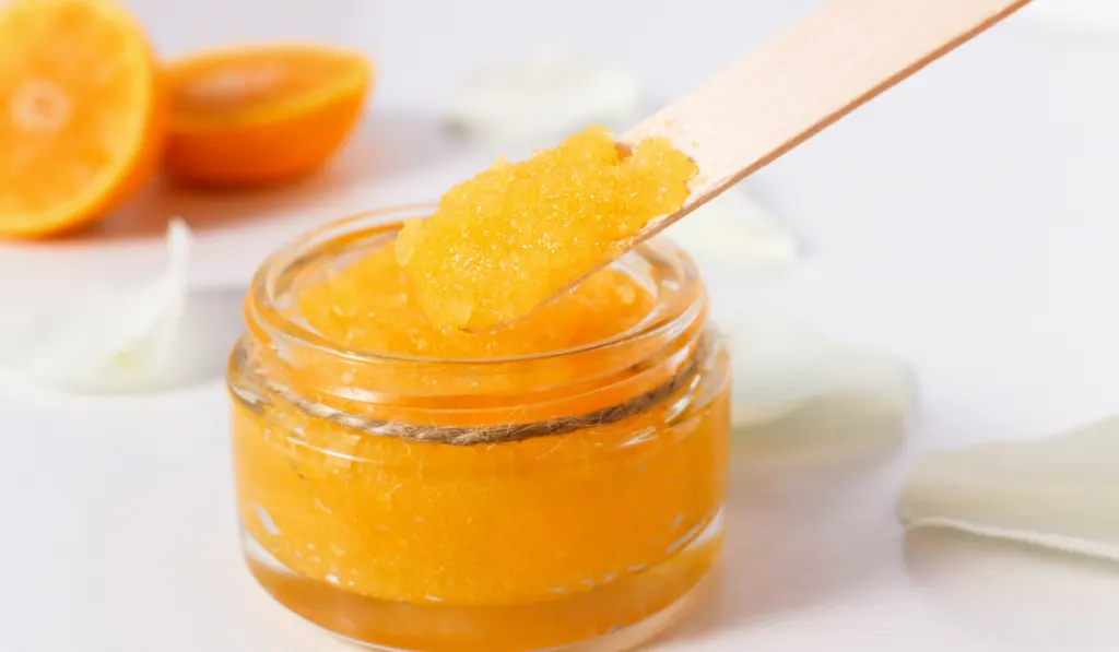 sugar body scrub with ripe, juicy oranges on a white wooden table.
