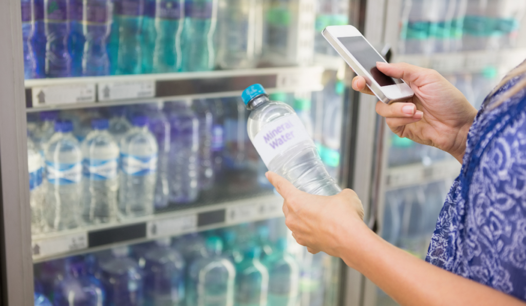 woman comparing the price of a bottle of water using her phone at the supermarket
