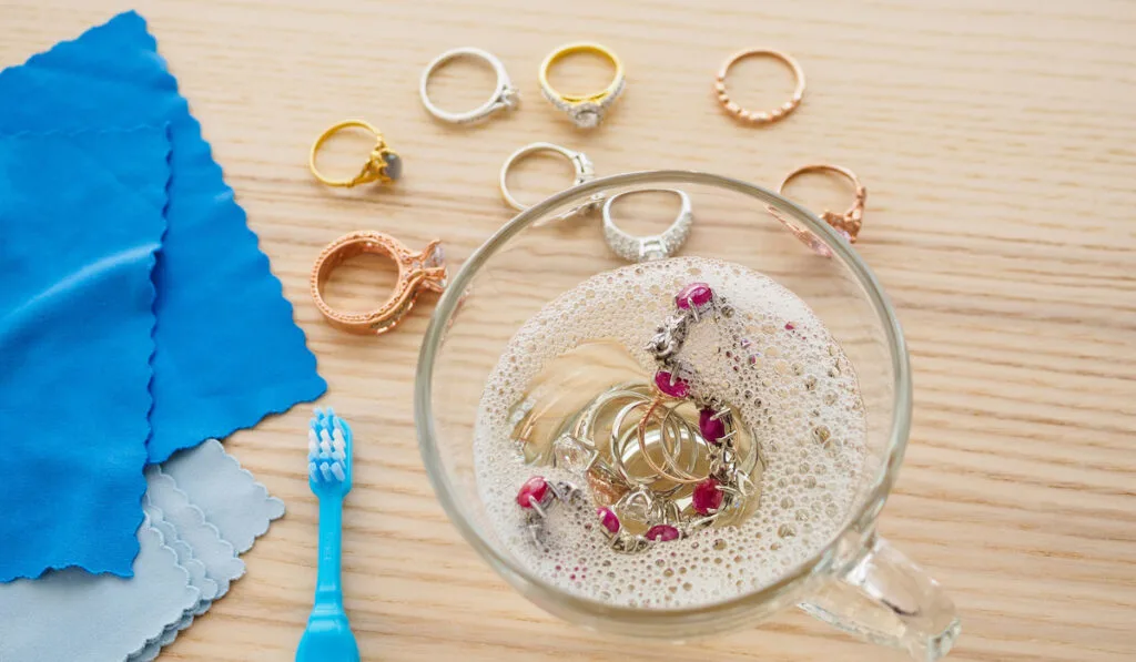 cleaning jewelry diamond ring with glass of hot water and dishwashing liquid on wooden table