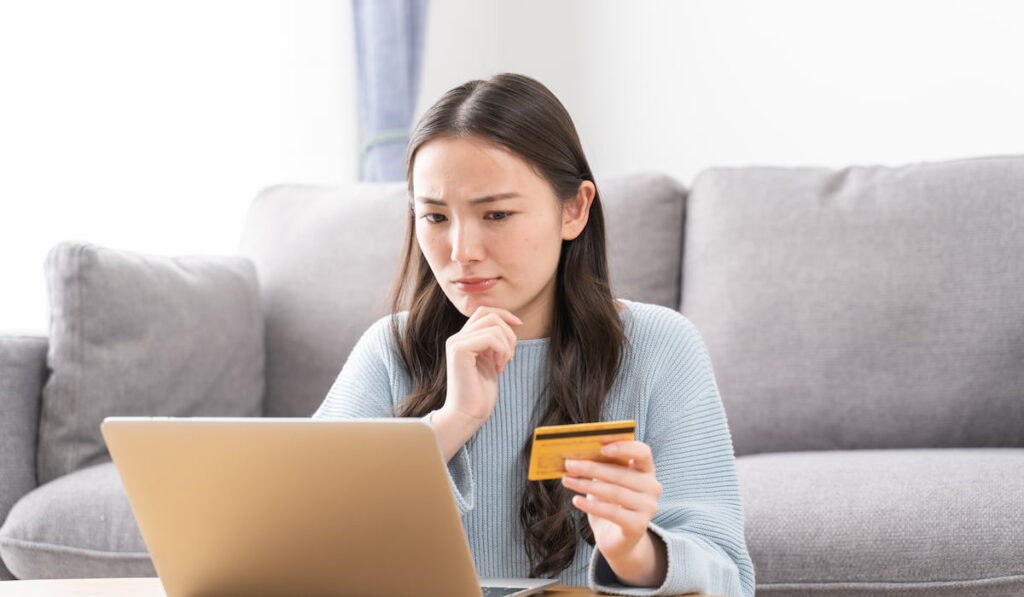 woman holding credit card while looking at her laptop monitor thinking of spending