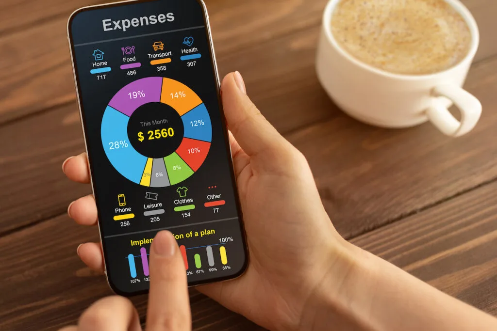 expense tracking concept using a budgeting app on woman's phone and coffee on wooden table