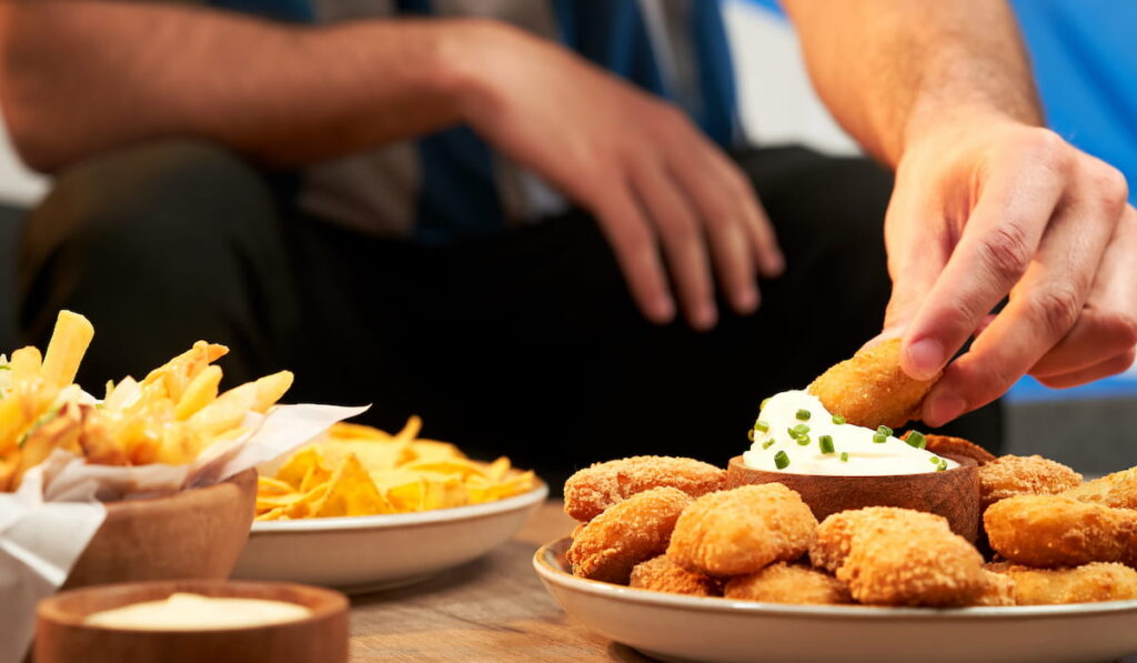 man eating finger foods, chicken nuggets with sour cream, fries and chips