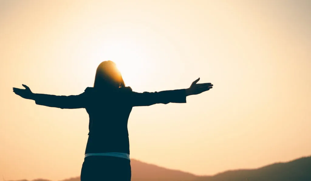 woman facing the sunset while her arms are wide open