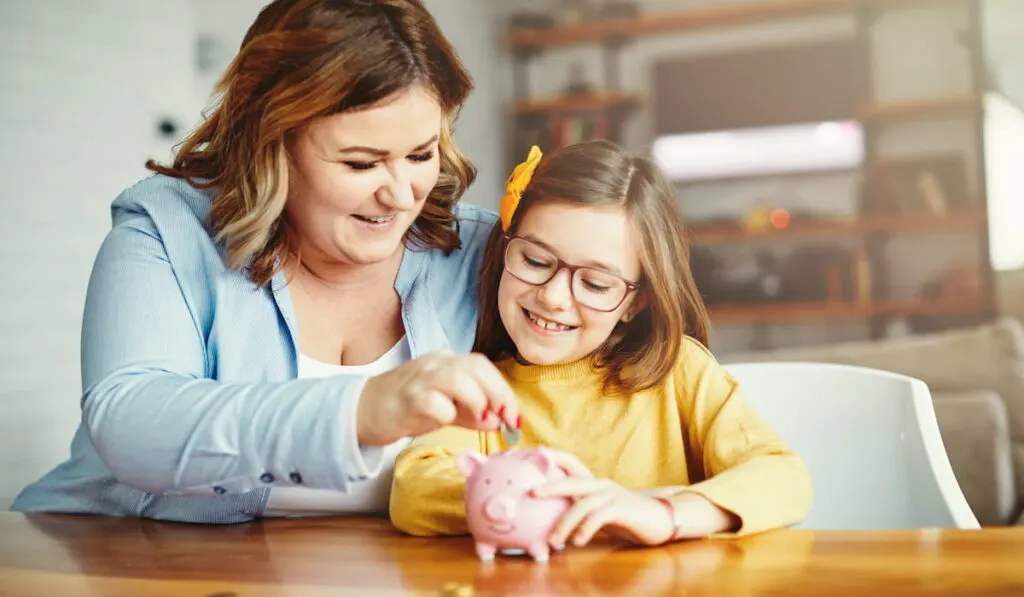 mother with daughter putting coin in piggy bank