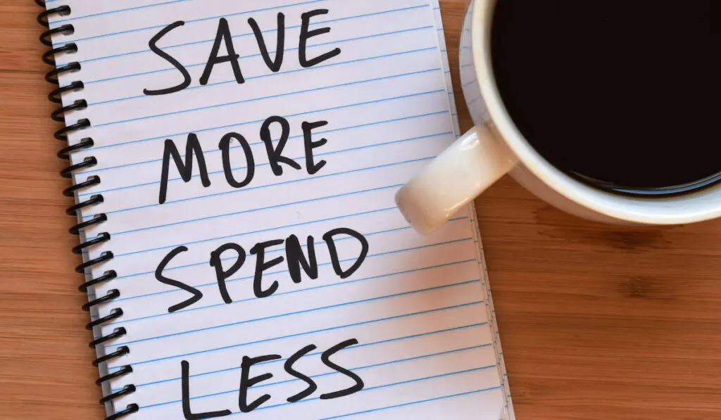 save more spend less written on notebook with a cup of coffee beside it