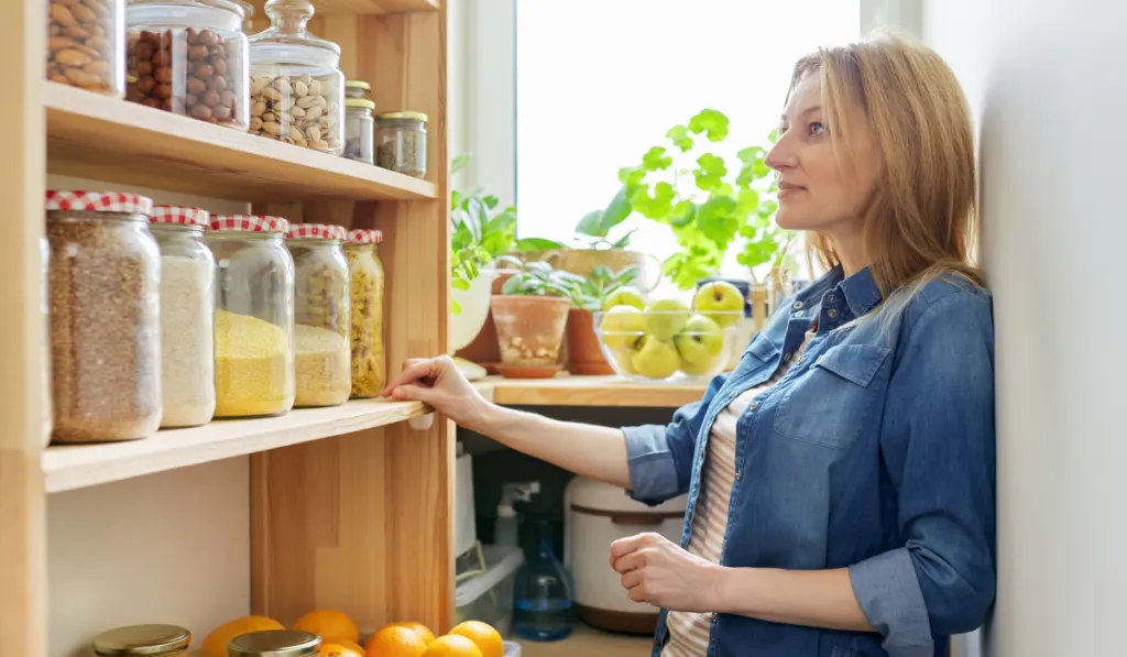 woman near wooden rack with food in jars and containers